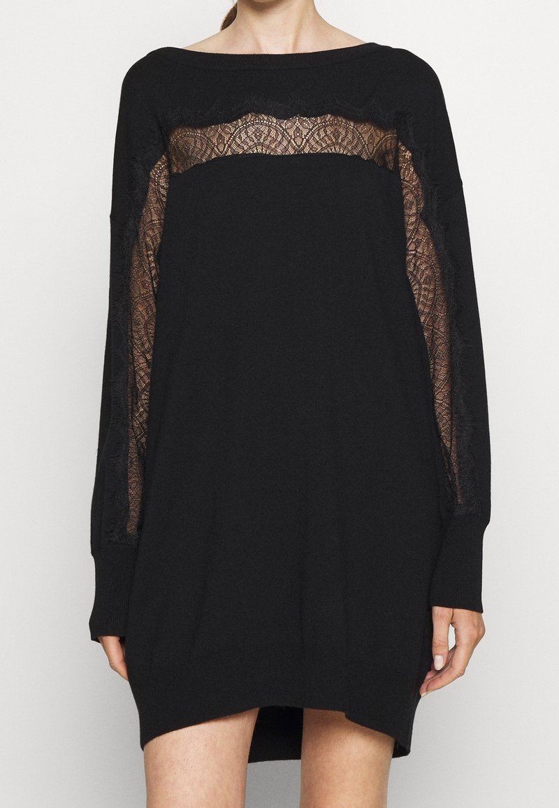 Robe noire oversize avec des panneaux en dentelle sur la poitrine et les manches, présentant une coupe ample et des manches longues. Matière en maille douce.