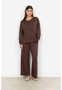 Set da salotto marrone realizzato in morbido tessuto. Presenta una maglia a maniche lunghe ample e pantaloni a gamba larga, entrambi dal design minimalista.