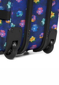 Maleta de ruedas con un patrón floral azul que presenta flores de múltiples colores vibrantes. Ruedas de plástico negras y acentos protectores en la base.
