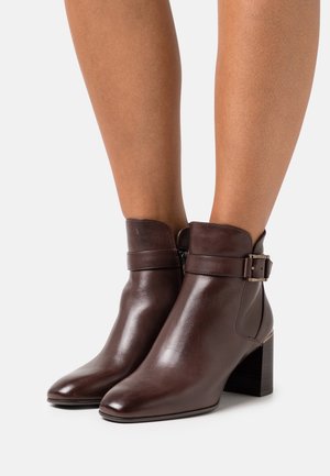 Bottes en cuir marron à la cheville avec un bout arrondi, détail de boucle sur le côté et un talon carré. Texture lisse avec une finition brillante.