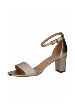 Sandal i metallisk guld med stropper, tykk blokhæls, bred forreste bånd og justerbar ankelrem. Glat tekstur og minimalistisk design.