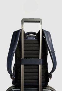 Mochila de cuero azul marino con respaldo acolchado, correas ajustables y un diseño elegante con un asa de metal para trolley que facilita su transporte.