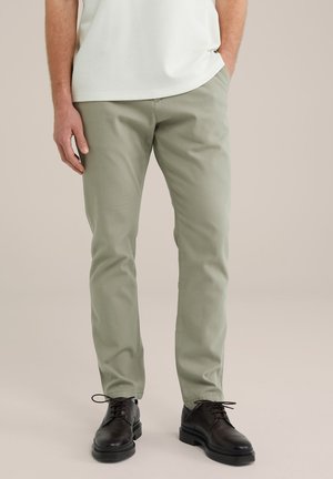 Pantalones de algodón verde claro con un corte recto, que presentan un acabado texturizado. Combinados con zapatos de cordones marrón oscuro.