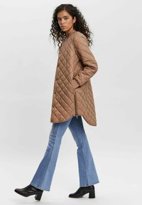 Brown quilted coat with a rounded neckline and side pockets, paired with light blue flared jeans and black heeled boots.