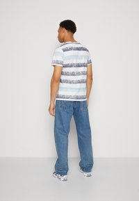 Camiseta a rayas en azul claro y marino, con cuello redondo y mangas cortas, combinada con unos vaqueros de mezclilla azul de corte holgado. Fondo blanco liso.