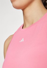 Pink athletic tank top made of lightweight fabric, featuring a round neckline and a white logo accent on the chest.