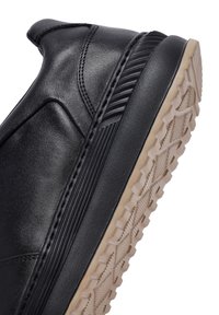Sneaker nera in pelle con finitura liscia, dotata di una robusta suola in gomma beige con un motivo di battistrada testurizzato per una migliore aderenza.