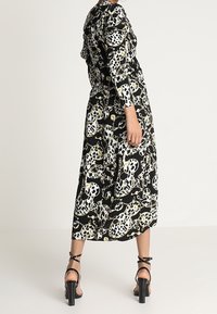 Robe noire midi avec des motifs floraux et de crânes blancs et jaunes, dotée de manches longues et d'un corsage ajusté, associée à des talons noirs à brides.
