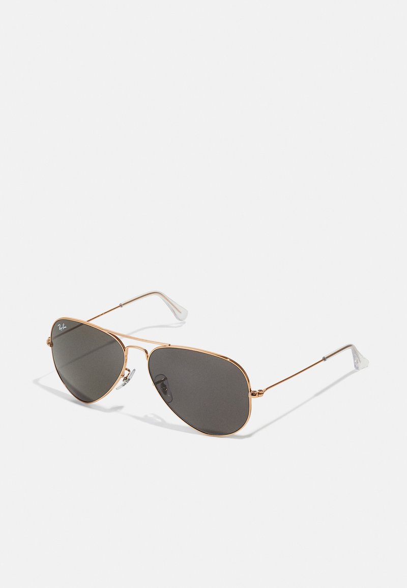 Ochelari de soare aviator din metal aurit cu lentile gri închis; au rame subțiri, pernițe nazale ajustabile și vârfuri pentru urechi translucide.