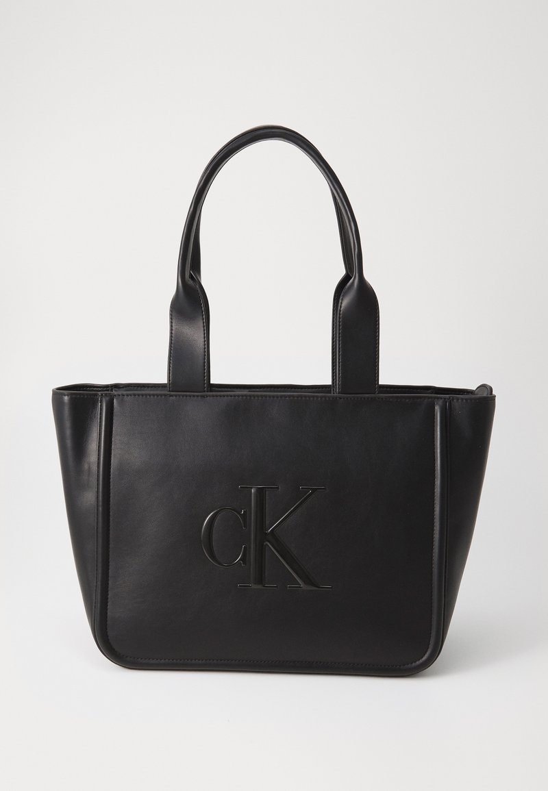Juodas odinis rankinis krepšys su dviem rankenomis; turi įspaustą "cK" logotipą; stačiakampio formos; lygus paviršius; minimalistinis dizainas.