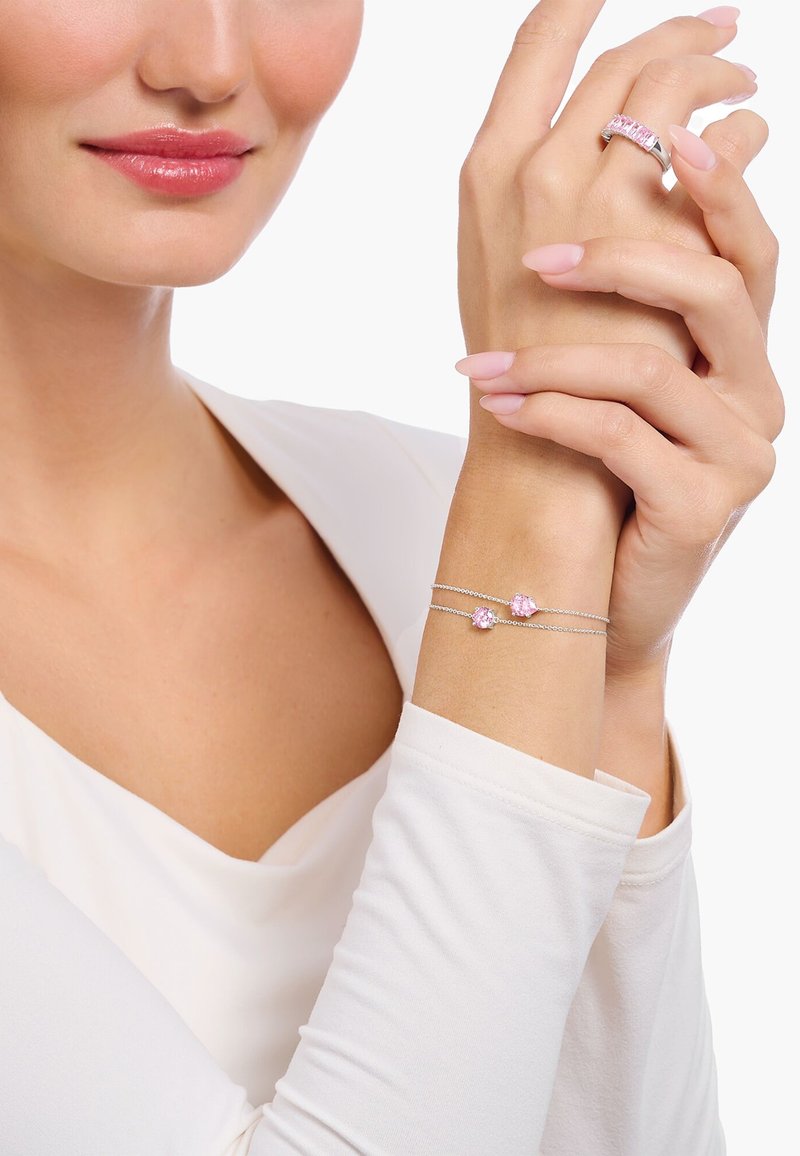 Bracciale d'argento con due accentuazioni di pietre rosa indossato su un polso, abbinato a un anello con gemma rosa coordinato. Luce soffusa e texture morbide.