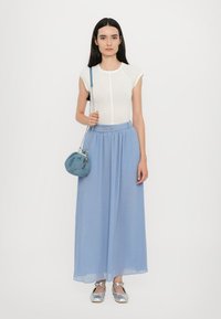 Biely priliehavý top, svetlomodrá maxi sukňa so záhybmi, strieborné topánky a okrúhla modrá crossbody taška so zlatým reťazovým popruhom.