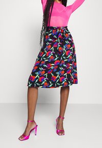 Gonna midi floreale con sfondo nero, caratterizzata da fiori rossi, blu e verdi, cintura legata e abbinata a tacchi a strappo rosa lucidi.