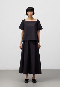 Mörk, texturerad tvådelsoutfit med en fyrkantig halsringning, kortärmad topp och en lång, flytande kjol, båda i en matchande djup nyans.