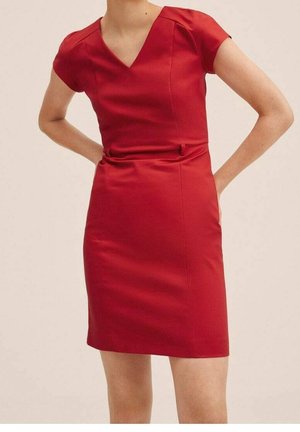 Woman wearing a fitted short-sleeve red dress with a V-neck, standing with hands on hips against a plain light background.