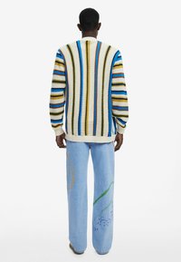Maglione lavorato a maglia multicolore con righe verticali, abbinato a jeans azzurri chiari con disegni botanici dipinti.