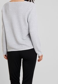 Harmaan raidallinen rento neulepusero, jossa pyöreä pääntie ja resorireunus. Yhdistetty mustiin, vartalonmyötäisiin housuihin. Pehmeä tekstuuri näkyy.