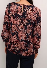 Blouse bleu marine à motif floral rose, manches longues, avec un détail en forme de trou à l'arrière. Confectionnée en tissu léger et lisse, avec des poignets élastiques.