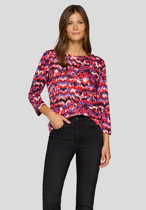 Bunt gestreiftes Langarmshirt mit einem wellenförmigen Muster in Rot, Lila und Weiß, kombiniert mit schwarzen engen Hosen. Glatte Textur.