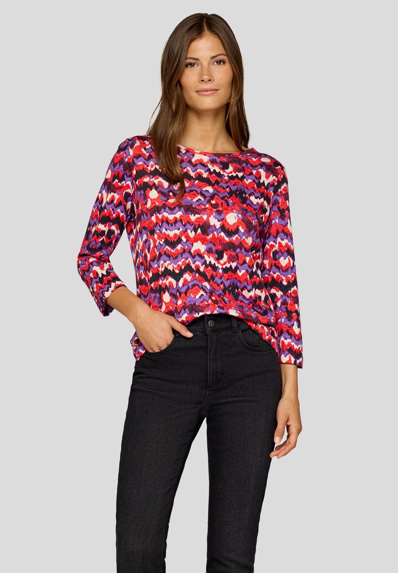 Multicolored long-sleeve top featuring a wavy pattern in red, purple, and white, paired with black fitted trousers. Smooth texture.