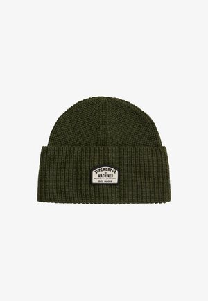 Gorro de punto acanalado verde oscuro con puño doblado y parche rectangular blanco que dice "Superdry Co. Machined Dry Goods."