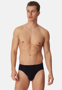 Slip neri da uomo realizzati in tessuto liscio; presentano un design aderente con cuciture a contrasto in vita e sulle gambe.