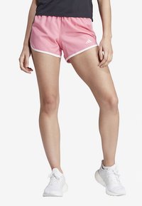 Calções esportivos rosa com acabamento branco e cintura elástica, feitos de tecido leve. Usados com tênis brancos.