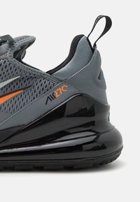 Grå och svart Nike Air Max 270 sneaker med orange swoosh och logotyp, mesh-överdela och stor synlig luftkuddenhet.