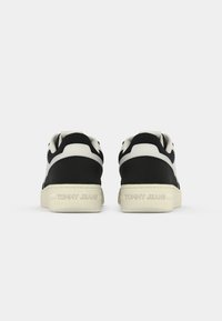 Paire de baskets noires et blanches vues de dos avec "Tommy Jeans" embossé sur les semelles blanc cassé.