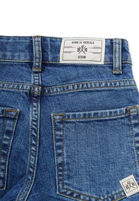 Farkut keskipitkällä sinisellä pesulla, joissa on vyötäröltä roikkuva "BAND OF RASCALS" -tagi. Näkyvissä on kontrastivärinen ommel ja kaksi takataskua.