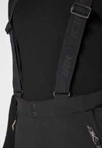 Schwarze Hosenträgerhosen aus strapazierfähigem Stoff, mit verstellbaren Trägern, zwei vorderen Reißverschlusstaschen und zwei Druckknöpfen an der Taille.