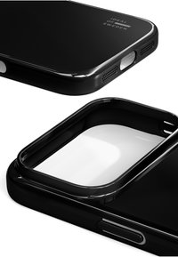 Musta puhelimen suojakuori kiiltävällä pinnalla, jossa on aukot painikkeille ja liitännöille, suorakulmainen muoto ja sileä pinta. Näkyvissä on Ideal of Sweden -brändäys.