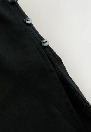 Juoda audinio medžiaga su lygiu paviršiumi, kartu su eile šešių tamsių sagų palei kraštą, kontrastine siūle ir šiek tiek išlenktu apatine kraštine.