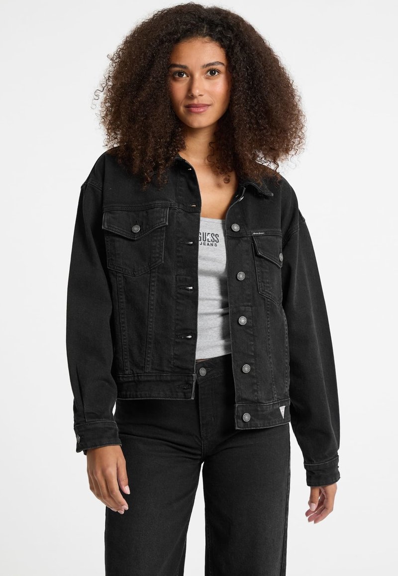 Black denim jacket with a relaxed fit, double chest pockets, silver buttons, and slightly tapered sleeves. Worn with a gray tank top and pants.