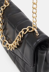 Bolso de mano de cuero negro acolchado con una correa de cadena dorada, que presenta una forma rectangular y un acabado suave y texturizado.