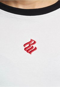White cotton t-shirt with a black ribbed crew neck, featuring red embroidered flame-like letters on the front.