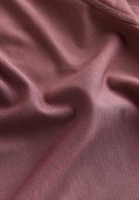 Miękka tkanina w kolorze łagodnego mauve o delikatnej, prążkowanej fakturze i widocznych przeszyciach, delikatnie złożona, ukazująca naturalne fałdy i szczegóły powierzchni.