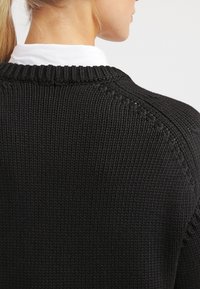 Schwarzer gestrickter Pullover mit rundem Ausschnitt und Rippdetails an den Schultern und am Ausschnitt, aus einem strukturierten Stoff.