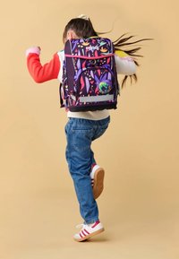 Child jumping with colorful floral-patterned backpack, wearing red and white sweater, blue jeans, and white sneakers with red stripes.