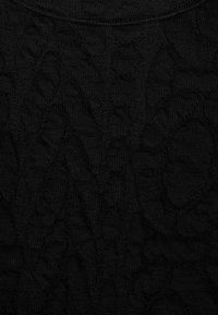 Tela negra con un patrón floral en relieve que presenta grandes hojas y pétalos en un material de punto texturizado.