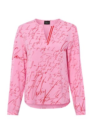 Blouse rose à manches longues avec un motif de script manuscrit rouge et une petite ouverture en V au niveau du col.