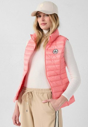 Roze gewatteerd vest met hoge kraag, logo-patch en grijs geribd shirt met lange mouwen. Heeft ook beige joggers met trekkoord en zwarte accenten.