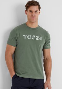 Green cotton t-shirt with a round neck and short sleeves, featuring "TOG24" printed in white on the front. Smooth, casual fit.