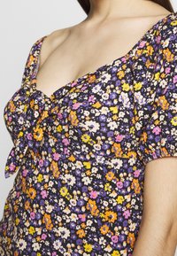 Květinové šaty s černým pozadím, zdobené drobnými květy v purpurové, oranžové, žluté a bílé barvě. Uvýjí se detail na výstřihu.