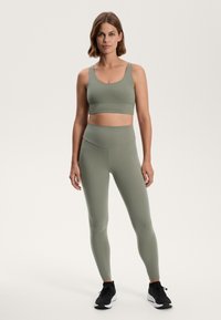 Green seamless bralette and high-waisted leggings made of smooth, stretchy fabric. Black athletic shoes complement the outfit.