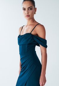 Teal avondjurk met een aansluitend lijfje, off-the-shoulder ontwerp, gedrapeerde stof en zijplooien, voorzien van dunne verstelbare bandjes.