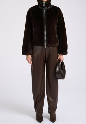 Brun faux fur jakke med høj krave, lynlåsfortil og læderdetaljer. Sammen med brune læderbukser og en rund håndtaske.