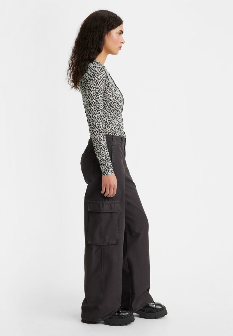 Haut à manches longues avec un motif floral noir et blanc, associé à un pantalon cargo noir à jambes larges avec poches latérales, et des chaussures noires massives.