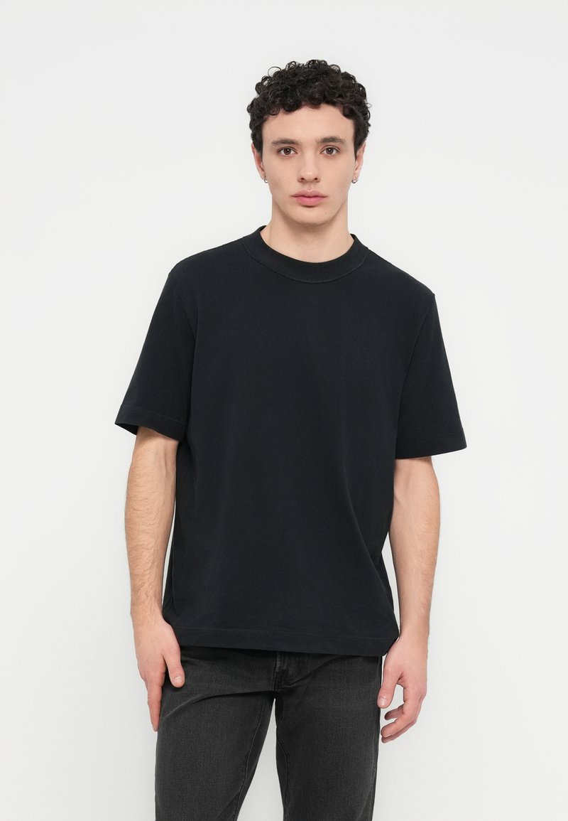 Μαύρο βαμβακερό T-shirt με στρογγυλή λαιμόκοψη και κοντά μανίκια. Μεγάλη εφαρμογή με απαλή υφή, συνδυασμένο με σκουρόχρωμο τζιν.