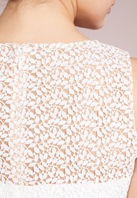 Vitt spetsklänning med ett detaljerat blommönster, sl ät textur och en diskret dragkedjeslutning i ryggen.